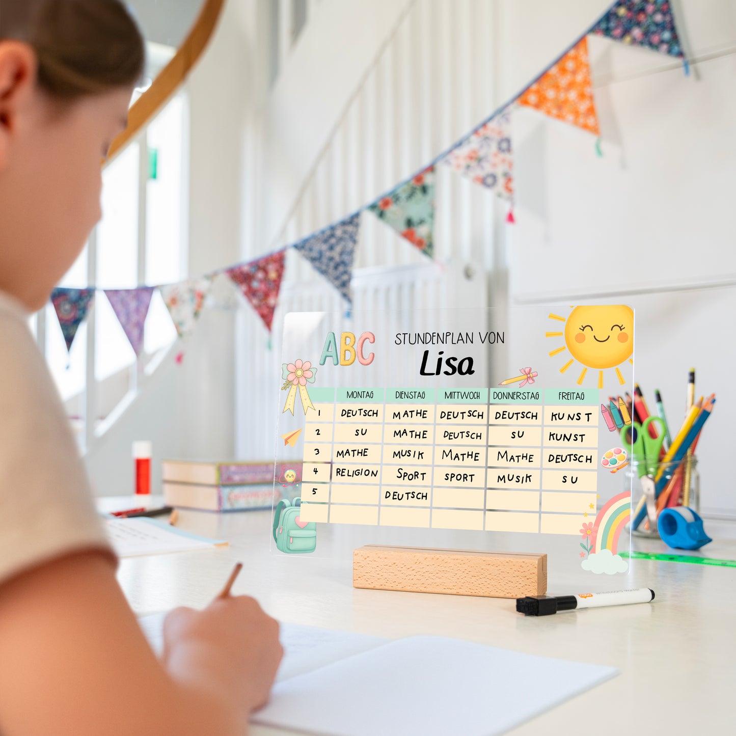 Kind sitzt am Schreibtisch, vor ihm ein personalisierter Acryl-Stundenplan mit Schulmotiv im Holzsockel, daneben ein Whiteboard-Stift